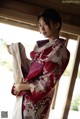 A woman in a red and white kimono standing by a window.