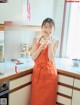 A woman in an orange apron standing in a kitchen.