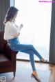 A woman sitting on a brown leather chair in front of a window.