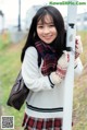 A young woman in a school uniform leaning against a pole.