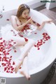 A woman sitting in a bathtub filled with rose petals.