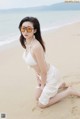 A woman in a white bikini sitting on the beach.