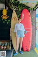 A woman standing next to a red surfboard in front of a building.