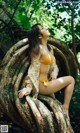 A woman in a yellow bikini sitting on a tree trunk.