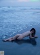 A naked woman laying on the beach next to the ocean.